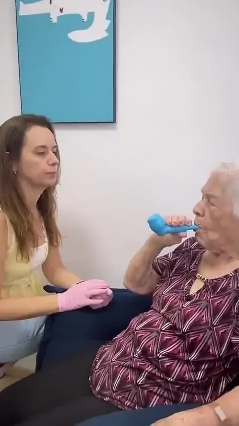 Profissional acompanha uma senhora idosa que sopra em um aparelho de exercício respiratório.