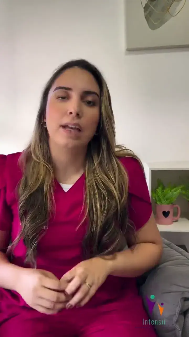 Fisioterapeuta de blusa rosa falando diante da câmera, em uma sala clara.
